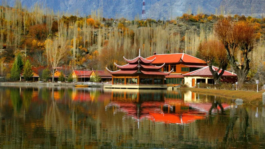 The Shangrila Resort in Skardu, Pakistan, with a traditional building reflected in the calm lake surrounded by autumn foliage.
