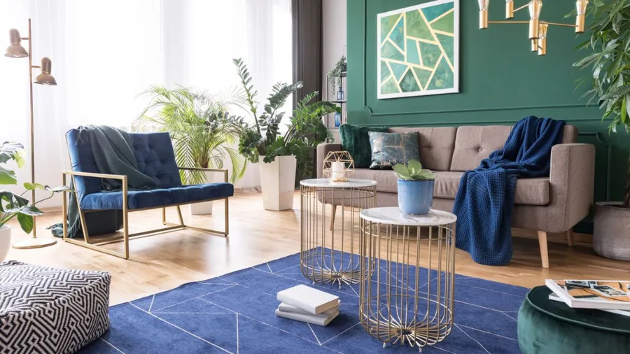 A bright living room with green walls, a beige sofa, blue armchair, and metal accents.