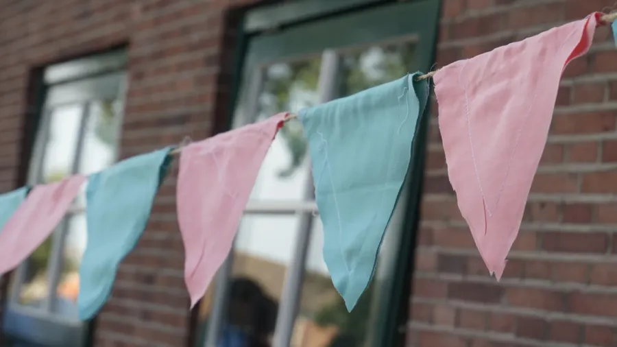 Pink and blue triangle, handmade cloth garland hung up as decoration, with brick building and old windows in the background. In Europe. Wedding decoration or gender reveal decoration.