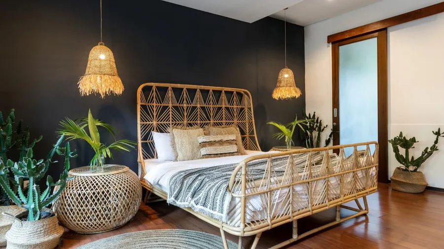 Rattan bed with hanging lamps and lush green plants creating a bohemian bedroom vibe.