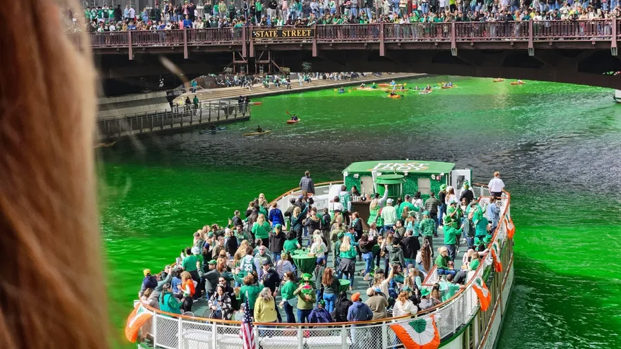 Chicago, Illinois, USA - March 15, 2025: POV from bridge of St. Patrick's Day celebrations with packed boat passing by in green-dyed Chicago River and crowded bridge.