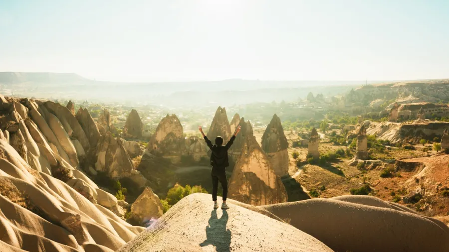 Female person stand with hands up over dramatic valley on hazy sunrise with fairy chimneys background. Solo exploration in Turkey. Cinematic Travel destination-Cappadocia 2020.