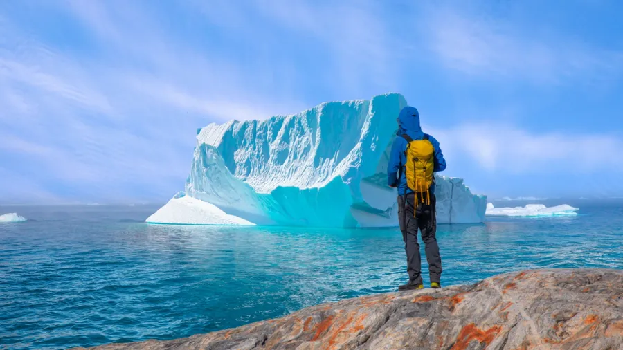 Environmental Concept - A Man Hiker looking at melting Ginat glacier - Melting of a iceberg and pouring water into the sea - Greenland - Tiniteqilaaq, Sermilik Fjord, East Greenland