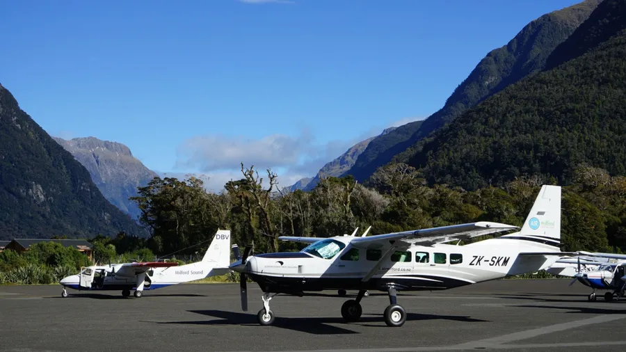 Editorial image of an Air Milford plane at Milford Sound Airport, New Zealand, photographed on April 15, 2023. The aircraft is set against the backdrop of Fiordland’s towering mountains