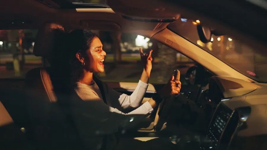 Singing, driving or happy woman in car at night, listening to radio or dancing for travel entertainment. Transport, music playlist or driver with sound system for fun, dark road or trip in vehicle