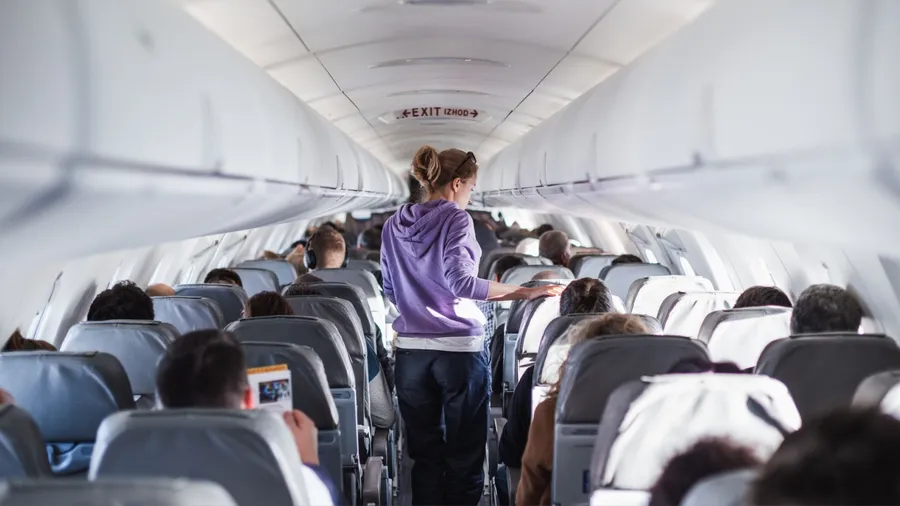 Interior of airplane with passengers on seats and female traveler walking the aisle. Commercial economy flight service concept