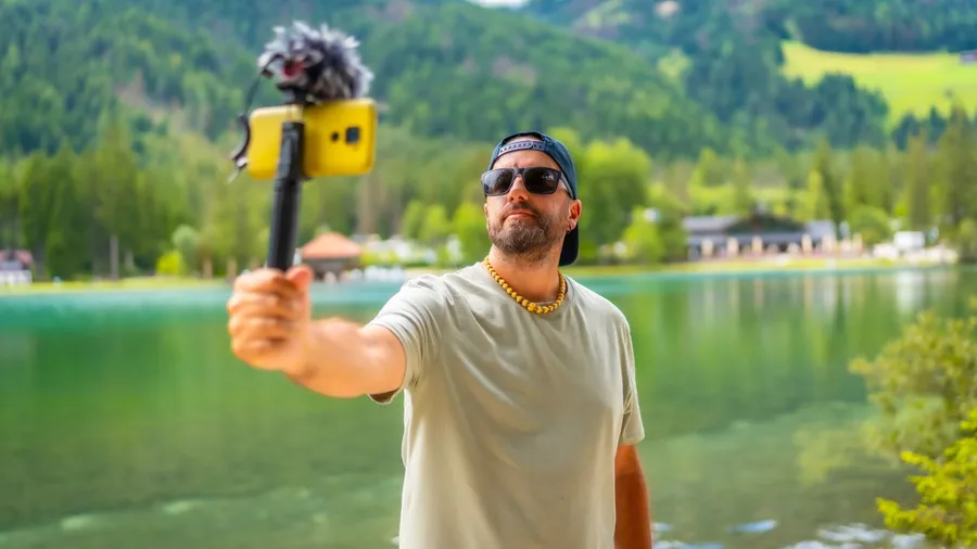Content creator filming a video with a smartphone and external microphone at lake dobbiaco in the italian dolomites during summer