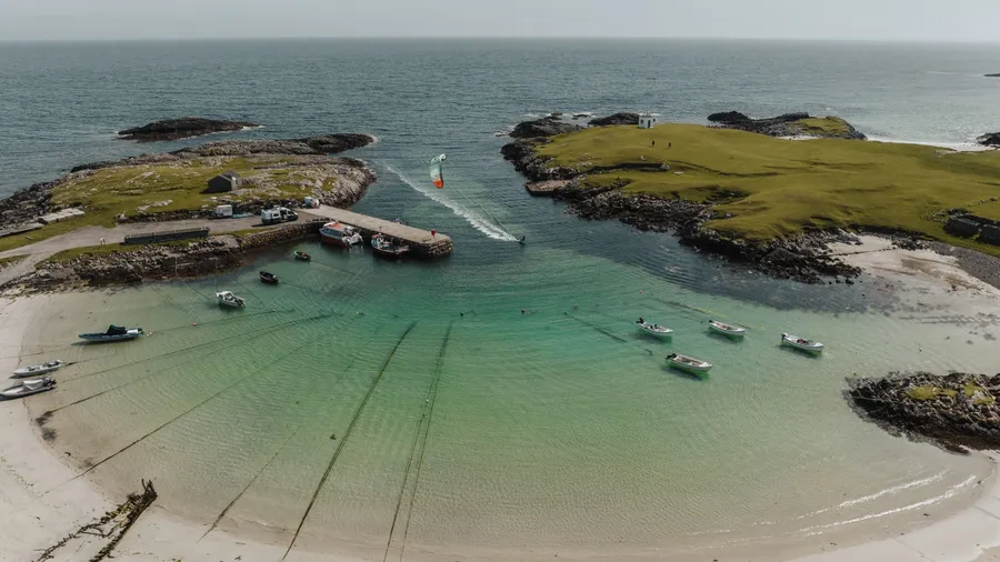 An aerial view of a kite surfer in water along Tiree island in Scotland with a sandy beach and seascape in the background