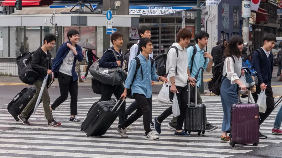 TOKYO, JAPAN - MAY 3RD, 2018. Japanese youth with luggage crossing the street in Shibuya.