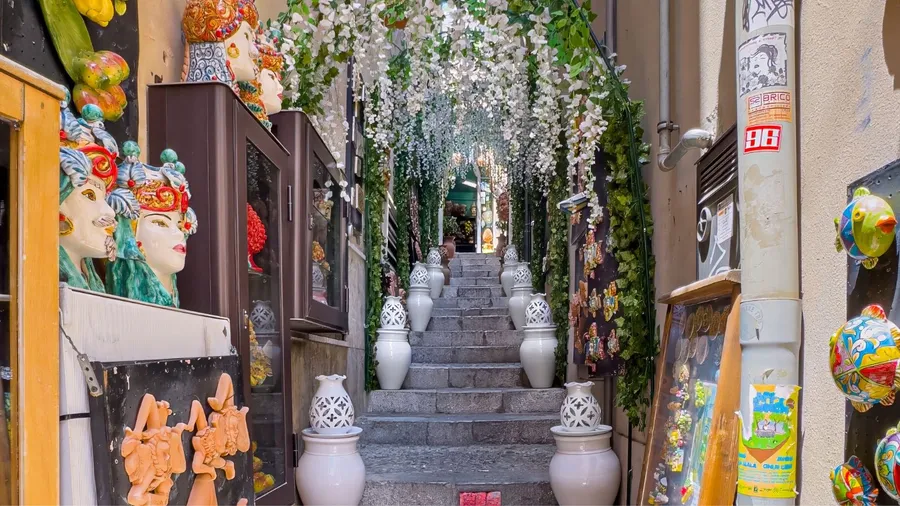 Vico Romano narrow alley with stairway up under bows of artificial white flowers. Colorful ceramic art pieces all the way
