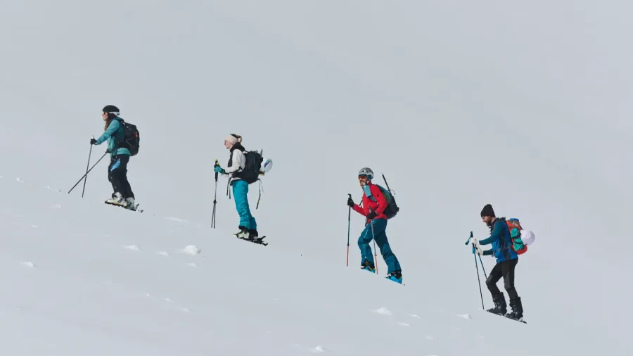 a group of professional ski mountaineers ascend a dangerous snowy