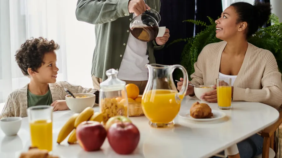 A family having breakfast at a table with fruits, juice and cereal, and pastries.