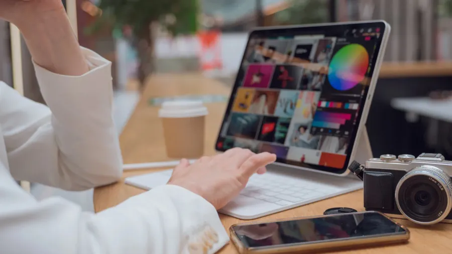 A designer working on her digital portfolio on a laptop with a camera and phone beside it.