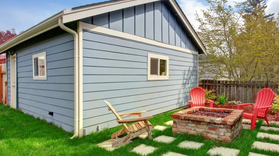 A garden with Adirondack chairs, firepit, stepping stones, and a pastel blue garden shed with window boxes.