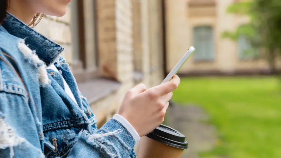 cropped view of cheerful student using smartphone and holding paper