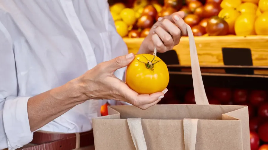 cropped view of mature woman putting yellow tomato into shopping