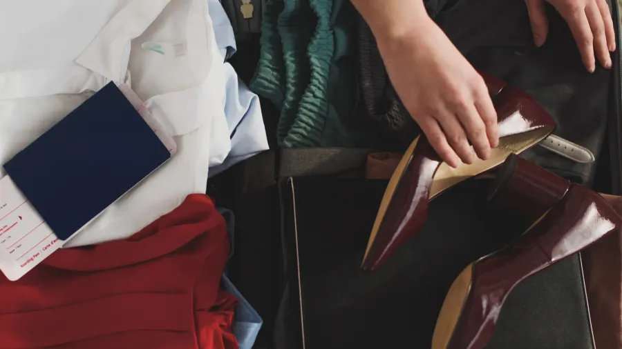 cropped view of woman packing clothes and passport in suitcase