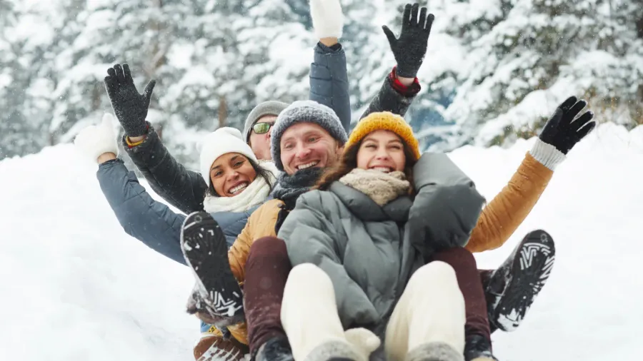 four funny friends in winterwear riding down hill in snow