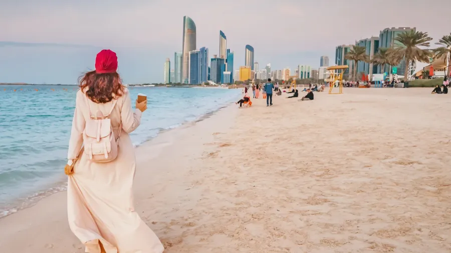 happy girl walking on sandy beach with takeaway coffee with