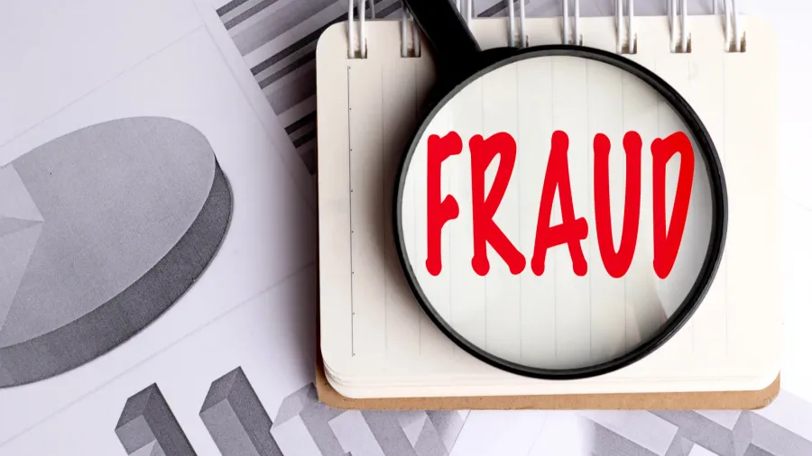 magnifying glass highlighting the word fraud on notebook with financial