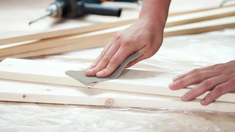 A man using a sand paper on a wood plank.