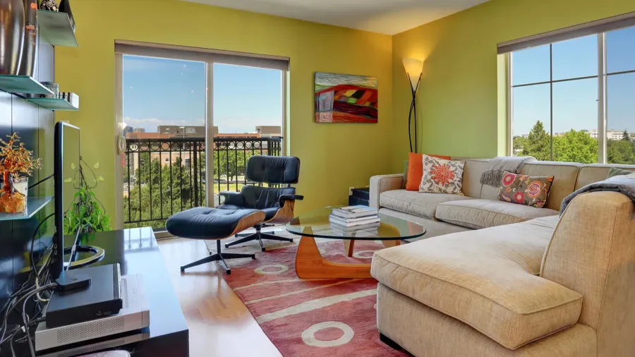 A modern living room interior with sectional sofa, glass top coffee table, media console table, wall sconces, and rug.