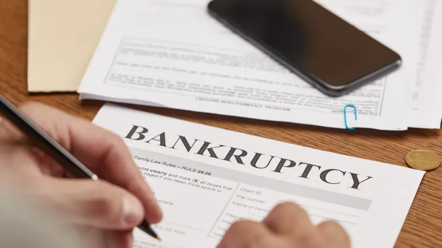 partial view of businessman filling in bankruptcy form at wooden