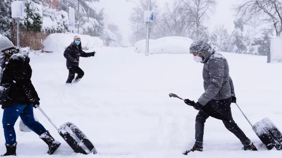 people carrying trolleys on a city street covered in snow