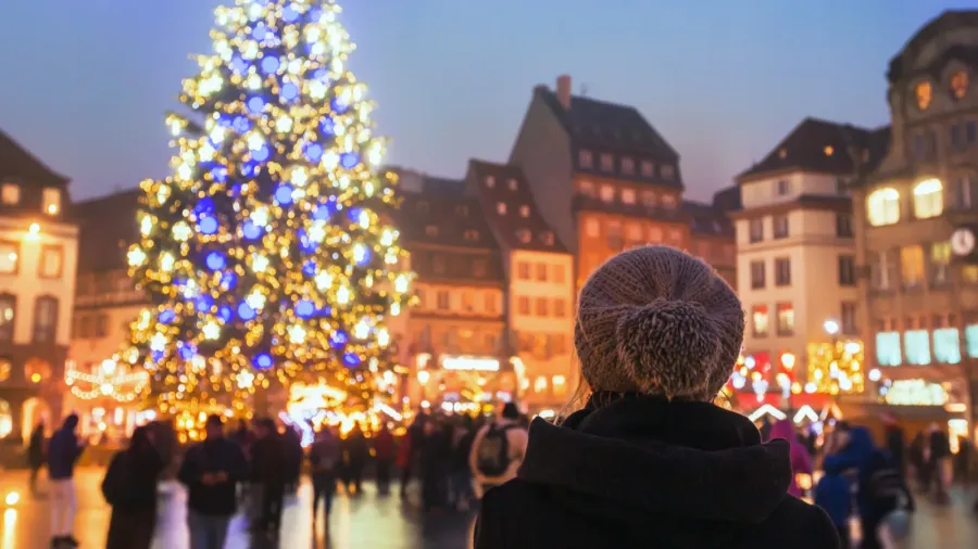 People in the Christmas market, a woman looking at the decorated illuminated tree in Strasbourg, France, Europe.