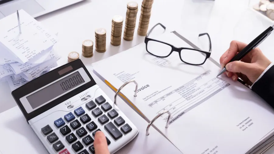 stacked coins and laptop in front of businesswoman calculating invoice
