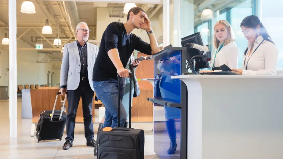 staff checking passport of male passenger at counter in airport