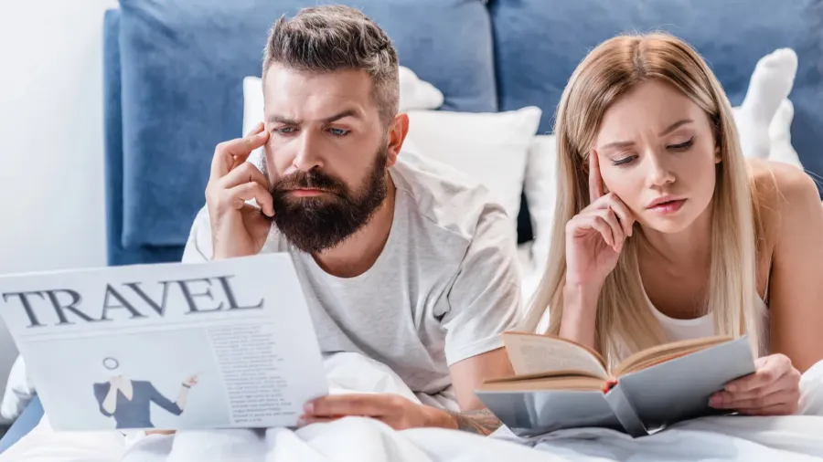 thoughtful man holding travel newspaper while pretty girl reading book
