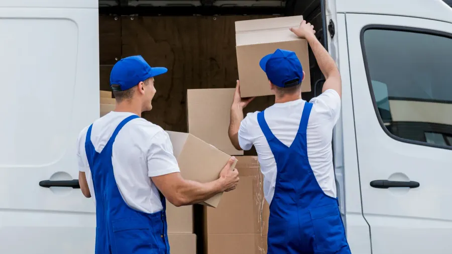 two removal company workers unloading boxes from minibus into new