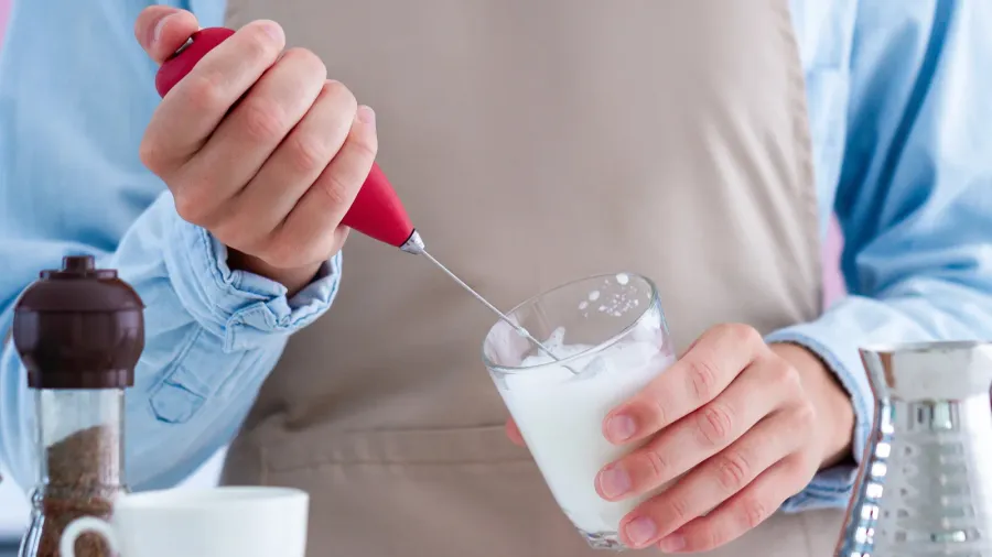 woman in apron making coffee with using a milk frother
