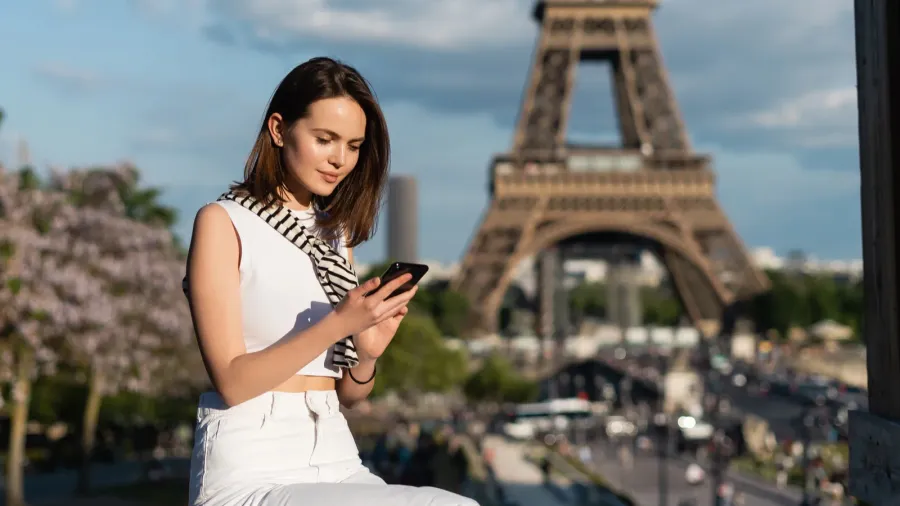 young woman in stylish outfit using smartphone while sitting near
